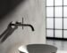 A matte black wall mount bathroom faucet installed above a white vessel sink on a wooden vanity, illustrating space-saving and modern design.